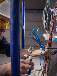 A male electrician works in a switchboard with an electrical connecting cable. A male electrician works in a switchboard with an electrical connecting cable, connects the equipment with tools.