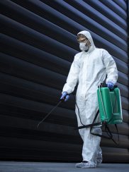 Person in white chemical protection suit doing disinfection of public areas to stop spreading highly contagious corona virus.